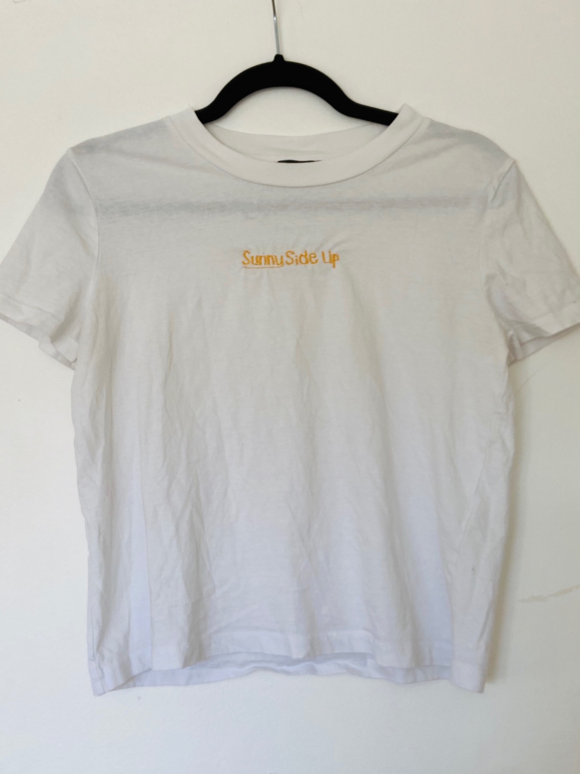 A white t-shirt on a hanger embroidered with the phrase 'Sunny Side Up'